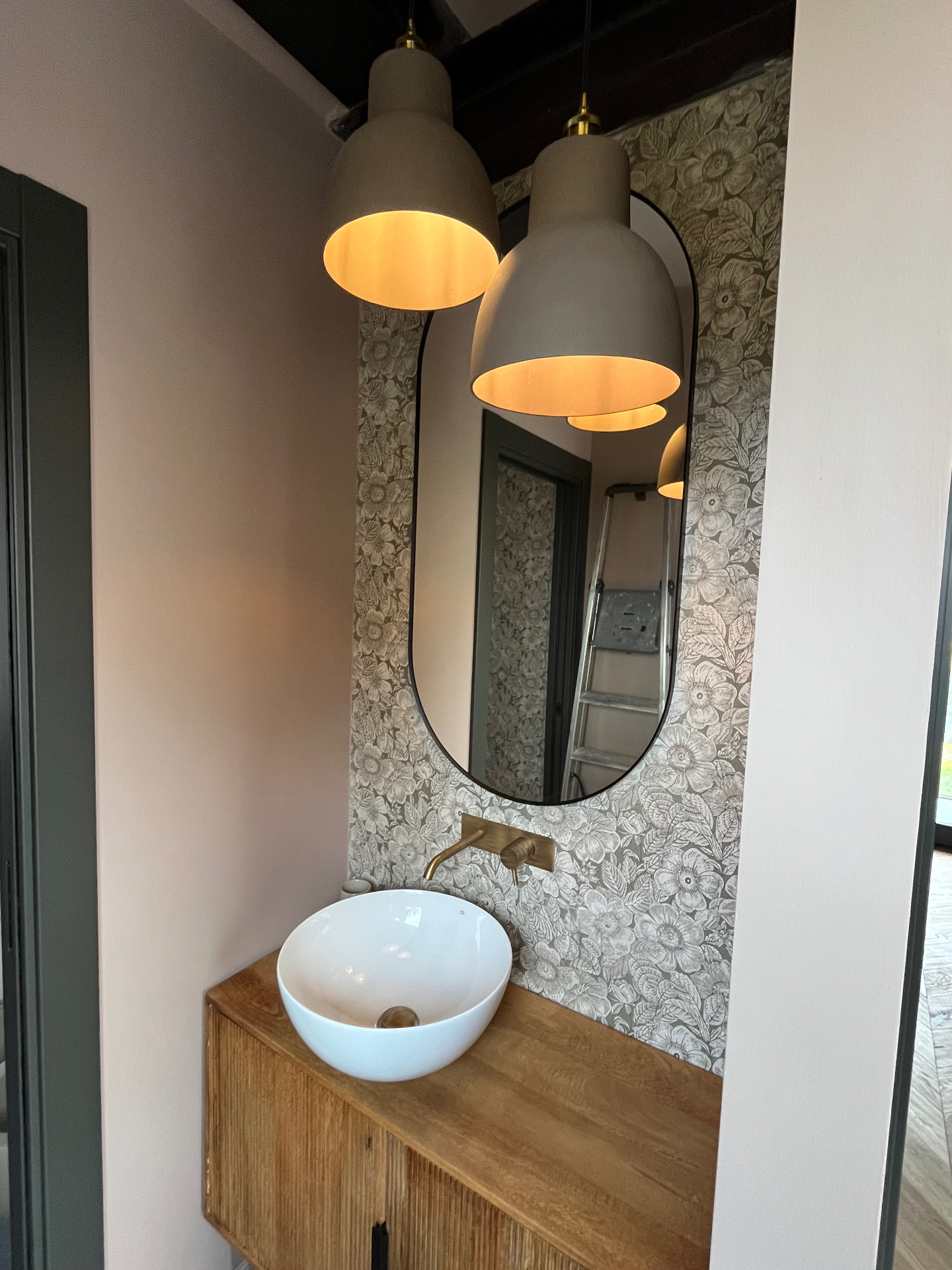 Designer bathroom with floral wallpaper, oval mirror and concrete pendant lamps